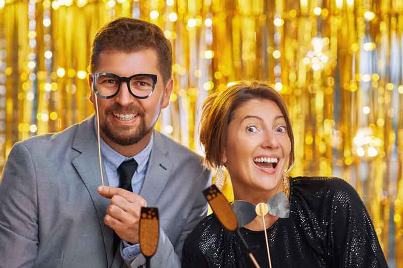 Couple posing with photo booth props against a gold shimmer backdrop.