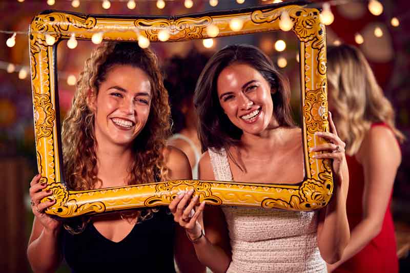 Two women laughing while holding a decorative photo booth frame.